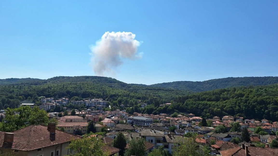 A large smoke plume rising from a wooded hillside above the town of Tryavna