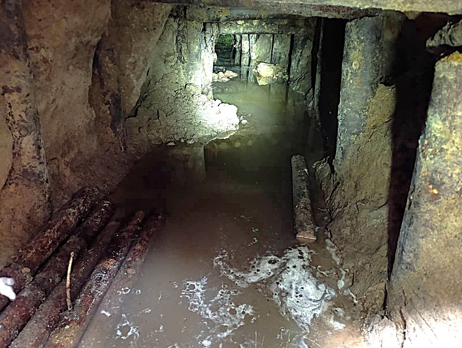 Inside the tunnel found near Piesčiai village, Varėna district, on 22 July 2026. The passage is approximately one metre in diameter, with wooden and metal supports visible along the walls and water on the floor. Photo: VSAT.